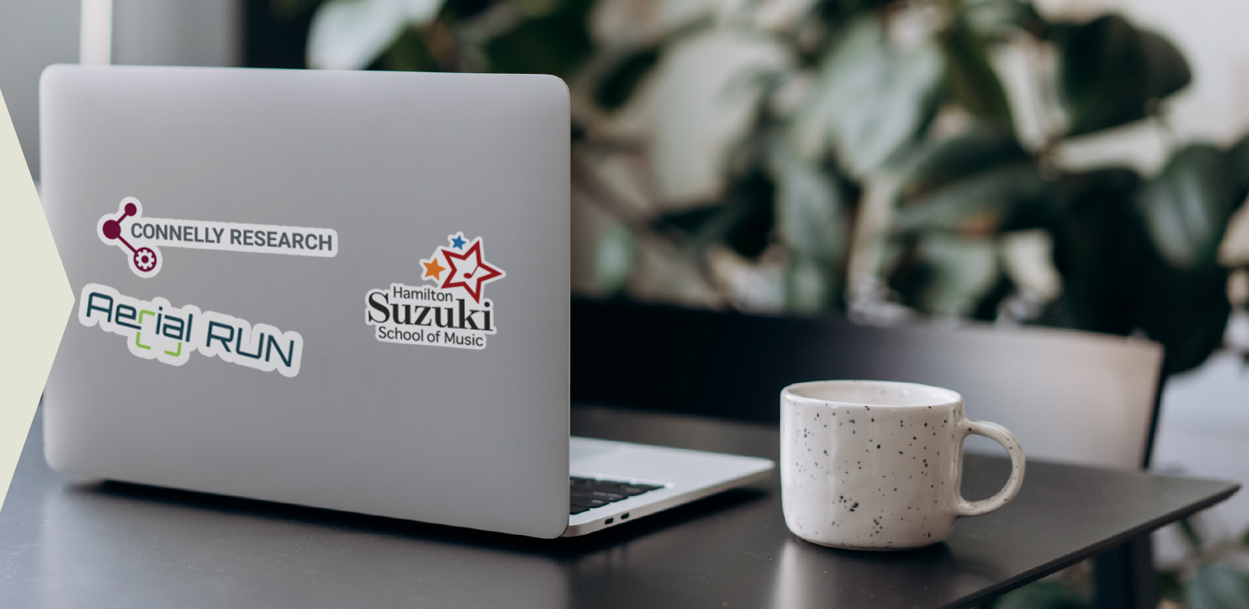 a laptop on a desk with the sickers of client logos; St. Charels Adult & Continuing Education, Gala Bakery, Hamilton Suzuki School of Music, McKeil Hamilton Philharmonic Orchestra, Good Shephard and Arial Run.