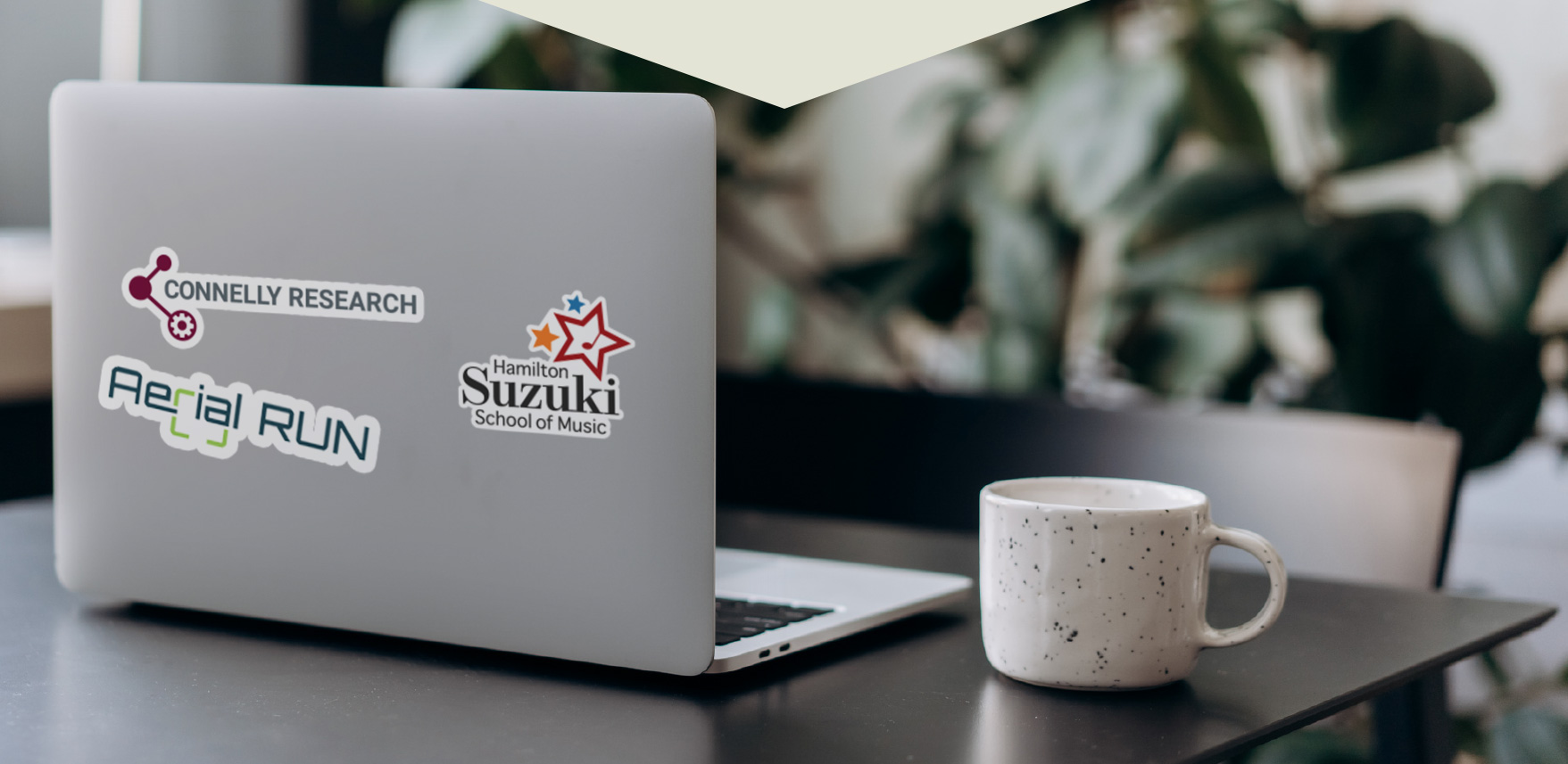 a laptop on a desk with the sickers of client logos; St. Charels Adult & Continuing Education, Gala Bakery, Hamilton Suzuki School of Music, McKeil Hamilton Philharmonic Orchestra, Good Shephard and Arial Run.